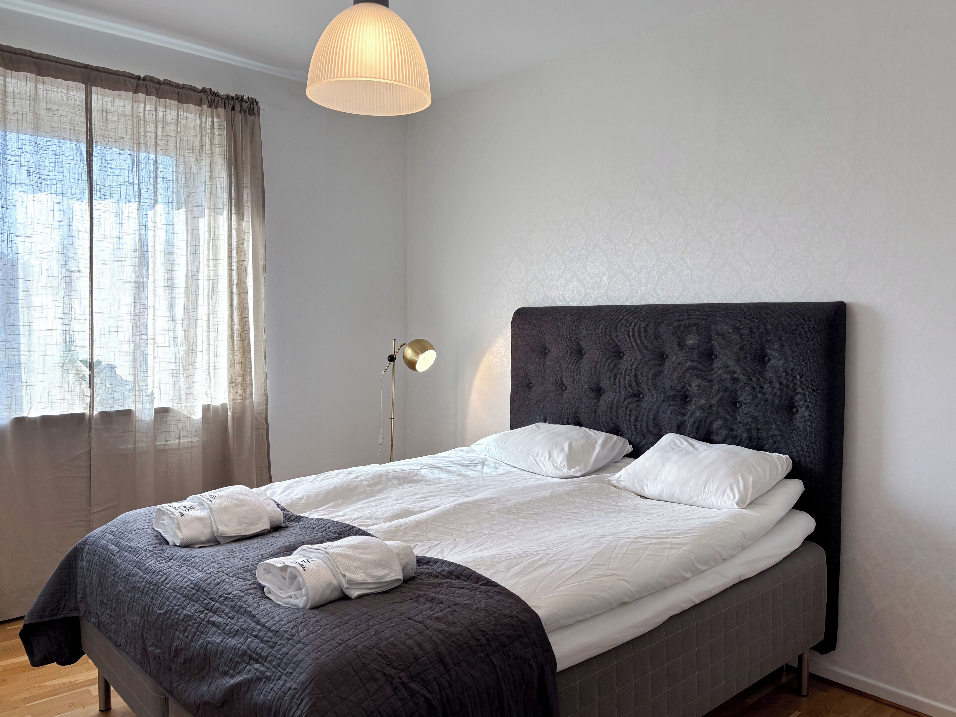 Un lit bien fait, avec du linge de lit blanc, une tête de lit sombre et une lampe de chevet.