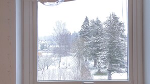 Una habitación con ventana que da a un paisaje nevado, una silla de madera y un radiador debajo de la ventana.