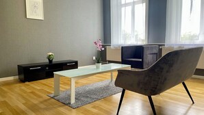 Una sala de estar moderna con una mesa de centro de vidrio, un sillón gris, un mueble negro y una planta en maceta.