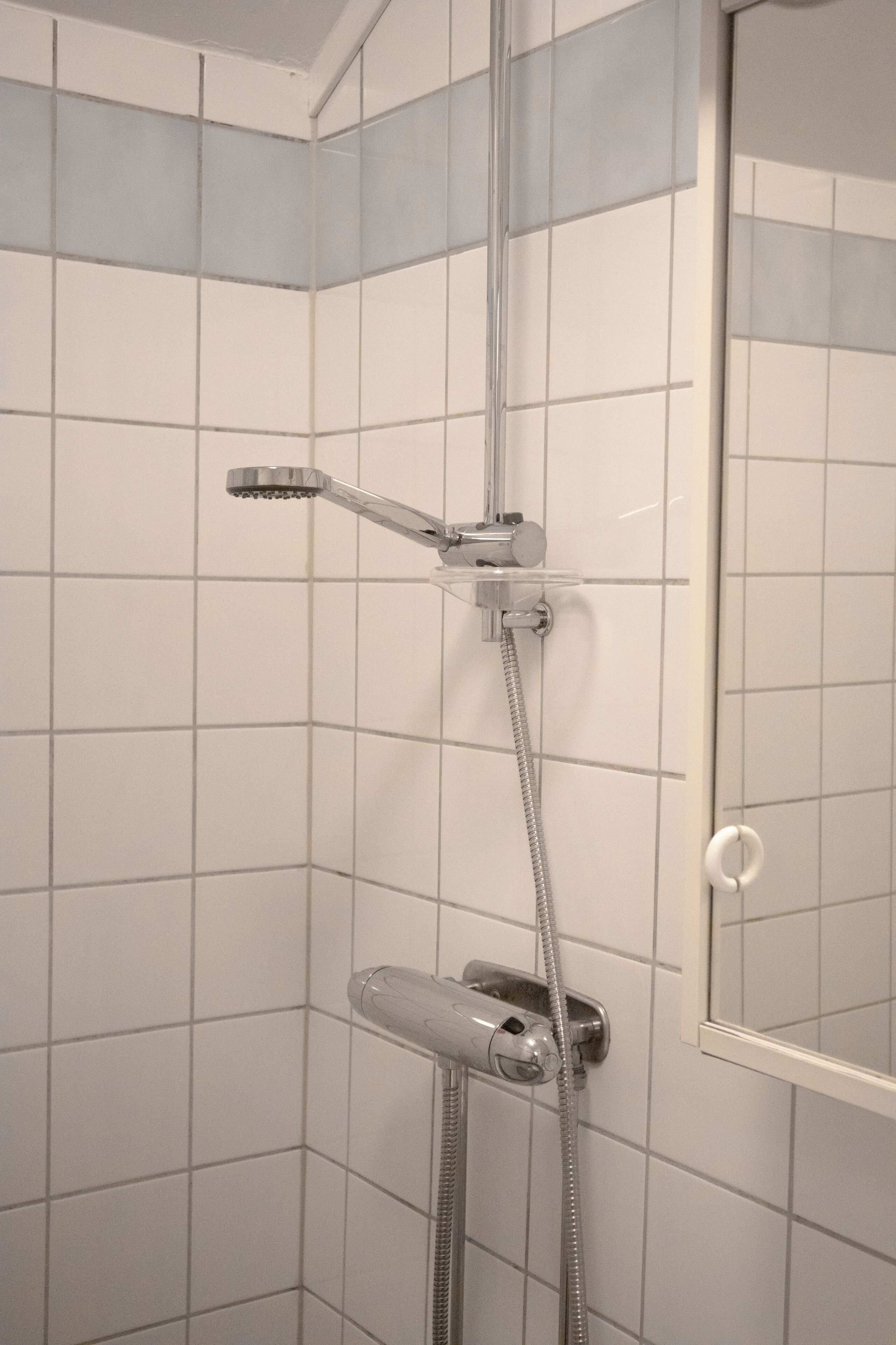En dusch med ett duschmunstycke som kan hållas i handen och en väggmonterad blandare.