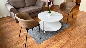 Una sala de estar con un sofá marrón, dos sillones marrones, una mesa de centro blanca y una orquídea en maceta.