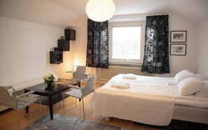 Habitación de hotel con cama, escritorio con silla, lámpara y ventana con cortinas.