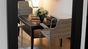 Una habitación con una mesa de comedor, dos sillas, un jarrón con flores, una lámpara y un espejo con marco negro.