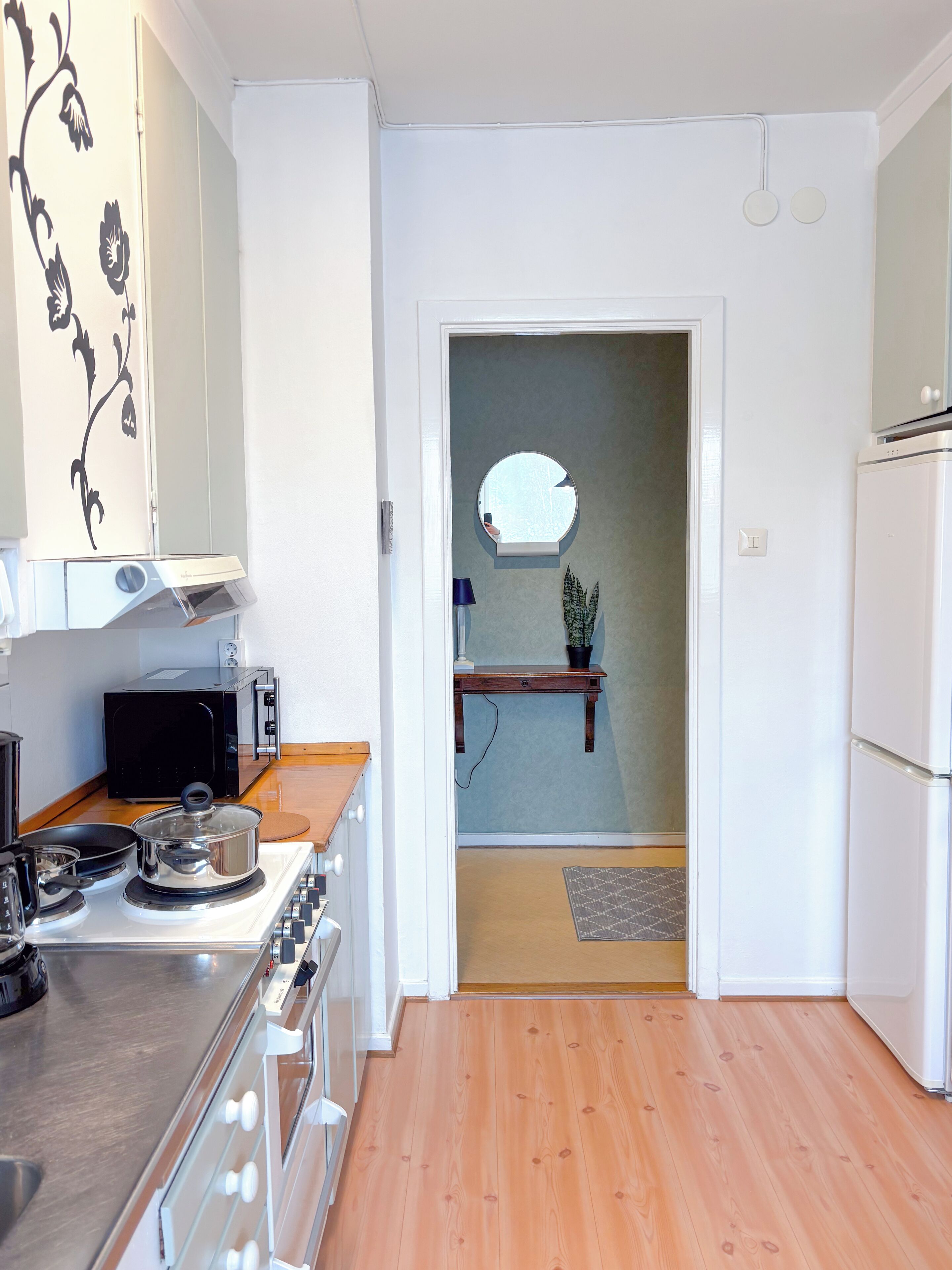 A kitchen with a stove, microwave, and refrigerator. There is a wooden floor and a door leading to another room.