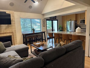 A modern living room with a fireplace, a dining area with a bar, and a kitchen with a sign reading 'SLUPES'.