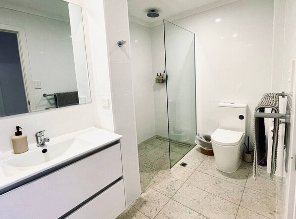 Une salle de bain avec un lavabo blanc, une cabine de douche en verre, des toilettes et un porte-serviettes.