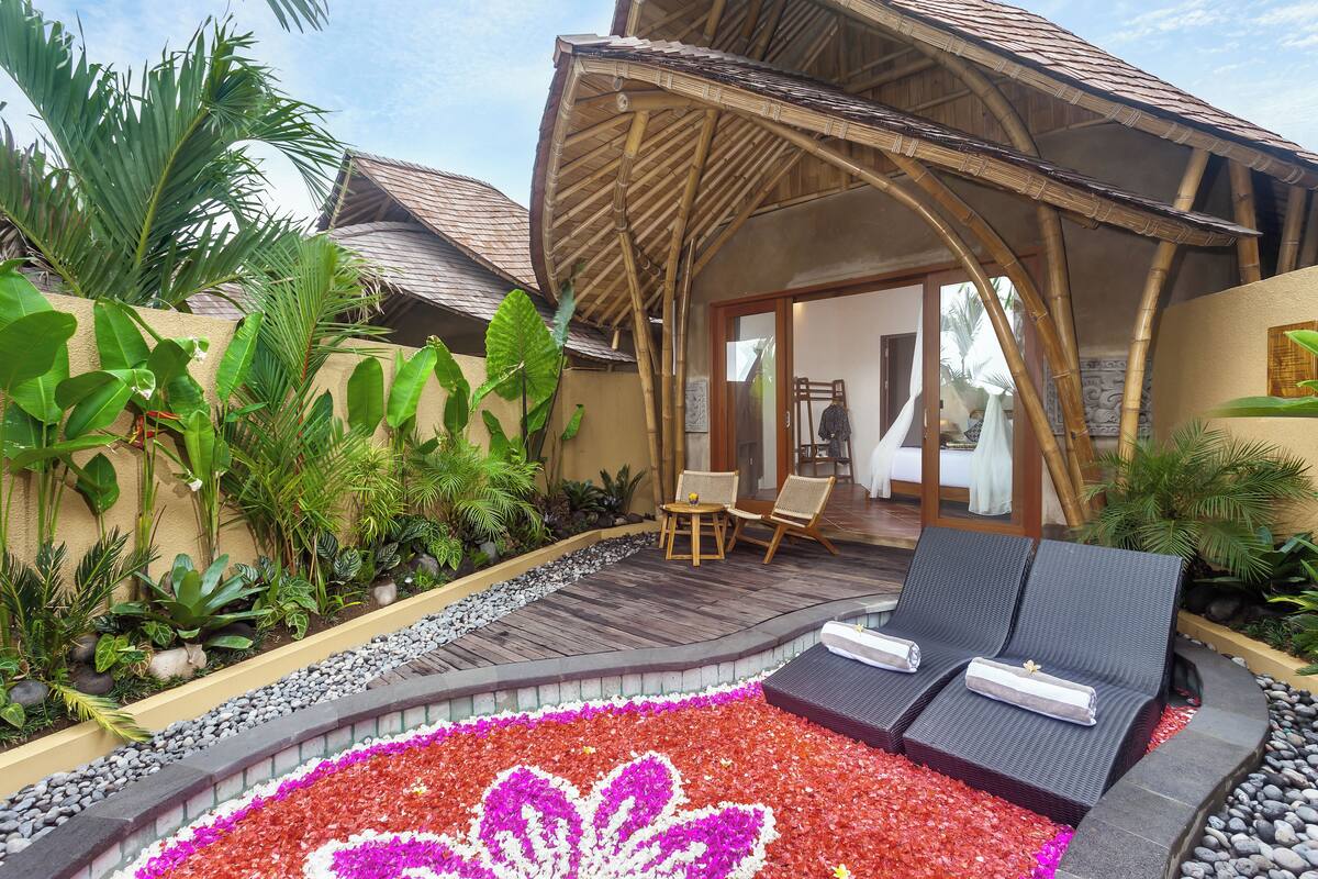 A resort with a covered outdoor seating area, a pool with a flower design, and lush tropical plants.