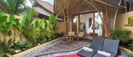 A resort with a covered outdoor seating area, a pool with a flower design, and lush tropical plants.