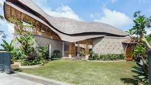 Una casa moderna con un tetto curvo originale, un ampio cortile e rigogliosa vegetazione tropicale.