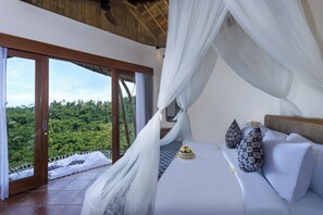 A bedroom with a canopy bed, a view of lush greenery, and a sliding glass door.