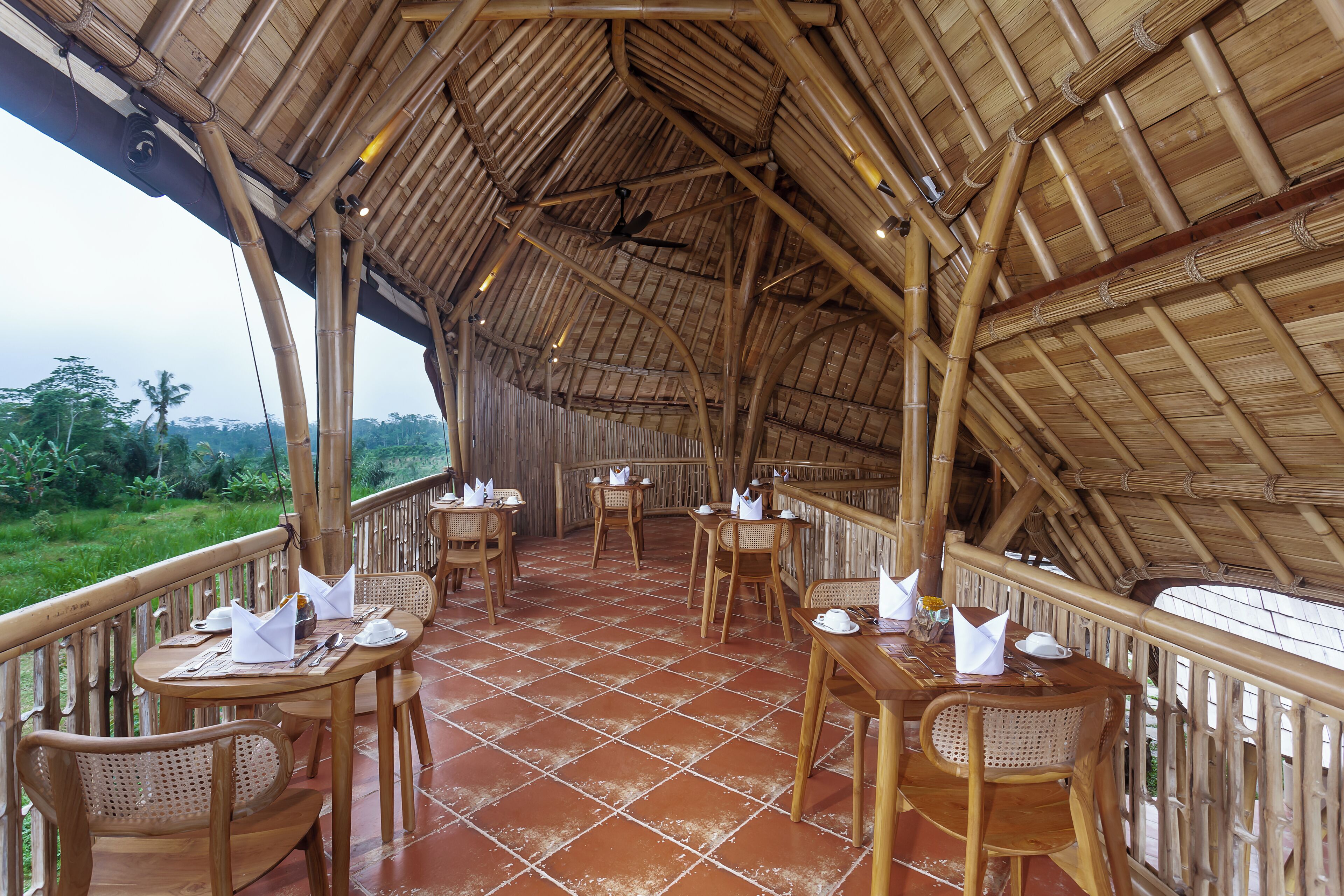An outdoor dining area with bamboo ceiling and walls, terracotta floor tiles, and wicker furniture.