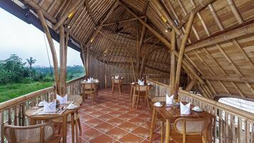 An outdoor dining area with bamboo ceiling and walls, terracotta floor tiles, and wicker furniture.