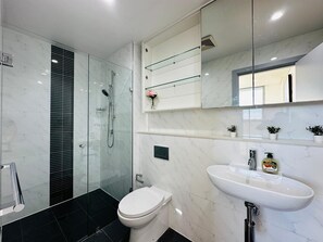 Une salle de bain moderne avec une douche à parois de verre, des toilettes blanches et un lavabo recouvert de carreaux de marbre.