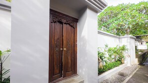 A traditional wooden door with intricate carvings, set within a white wall. - Pondok Merta-Two Bedroom Pool Villa Ubud (Ubud)