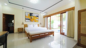 A modern bedroom with a large bed, a wooden nightstand, a bedside table, a wall-mounted abstract painting, and a sliding glass door leading to a balcony. - Pondok Merta-Two Bedroom Pool Villa Ubud (Ubud)