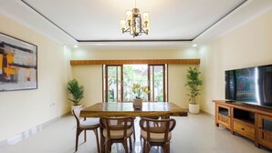 A spacious dining area with a wooden table and chairs, a chandelier, and a television on a wooden cabinet. - Pondok Merta-Two Bedroom Pool Villa Ubud (Ubud)