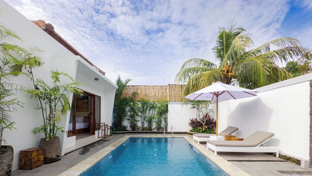 A swimming pool with tiled flooring, white walls, and a wooden deck. There are lounge chairs and a wooden fence in the background. - Pondok Merta-Two Bedroom Pool Villa Ubud (Ubud)