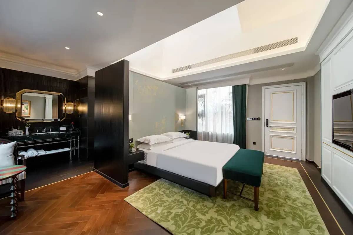 A modern hotel room with a bed, bedside table, and a desk with a chair.