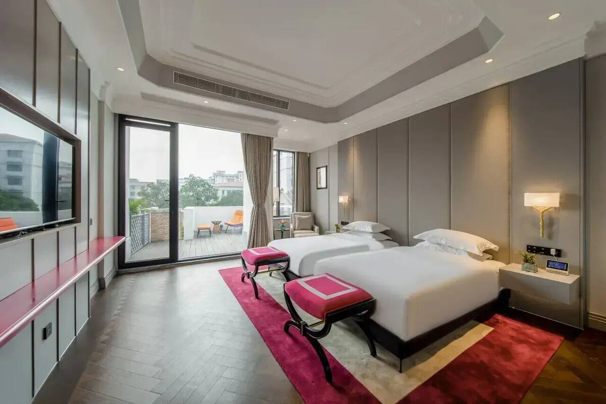 A hotel room with two beds, a TV, a balcony, and a view of the city.