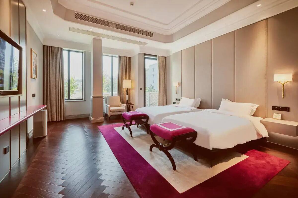 A hotel room with two beds, a desk, a chair, and a TV.