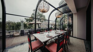 An outdoor dining area with a table set for four, surrounded by red cushioned chairs, under a glass enclosure with decorative hanging lights. - Seclusion with the mountain (Wuhan)
