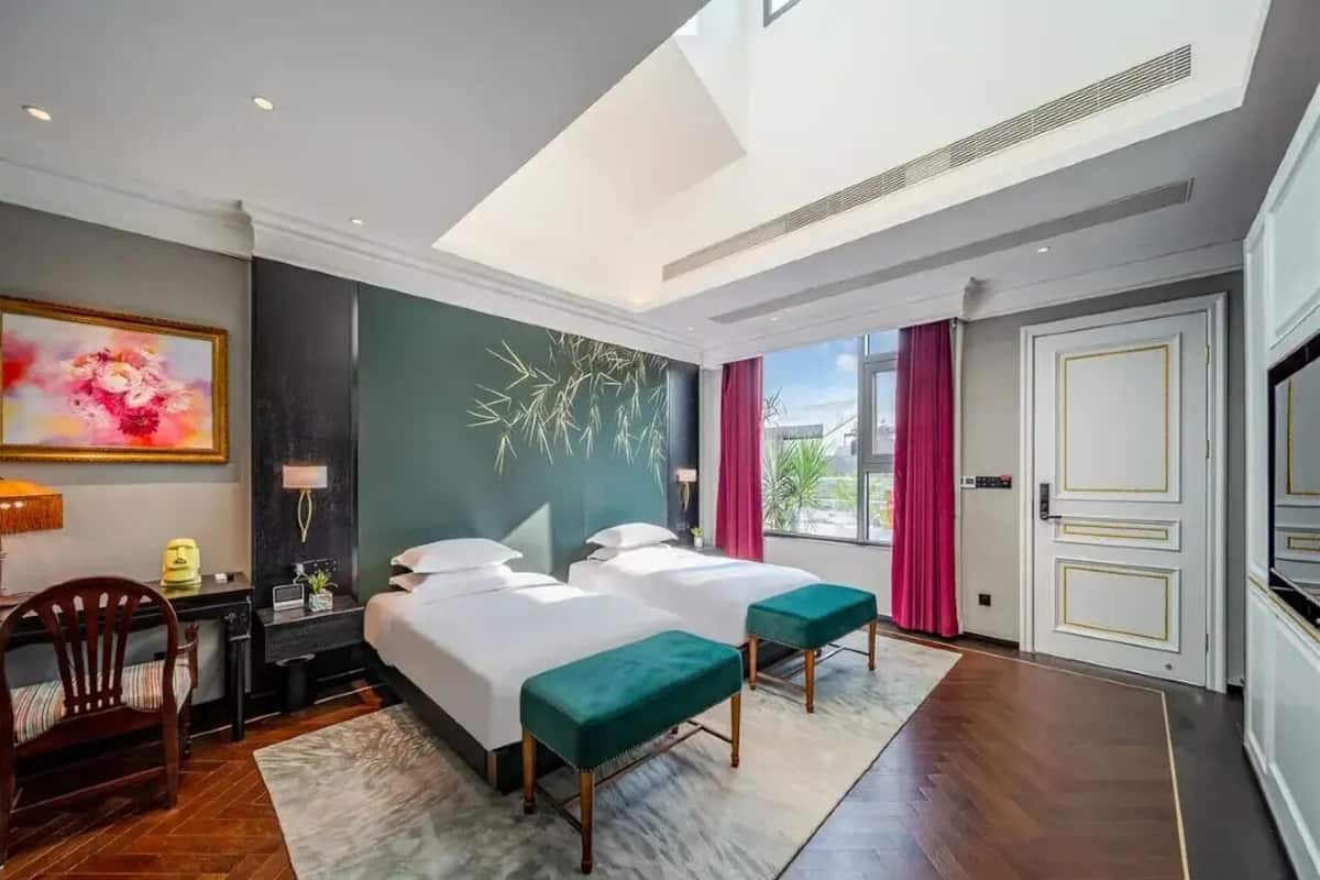 A hotel room with two beds, a desk, a chair, and a large window with curtains.