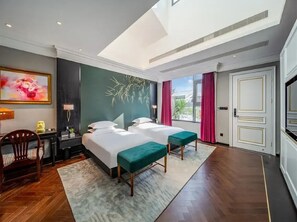 A hotel room with two beds, a desk, a chair, and a large window with curtains.