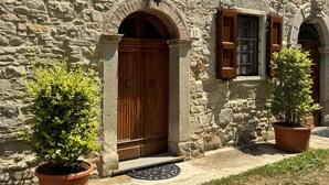 A stone building with a wooden door and window shutters, potted plants, and a stone wall.