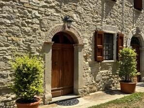 A stone building with a wooden door and window shutters, potted plants, and a stone wall. - Il Rifugio - Cottage with Pool (Emilia-Romagna)