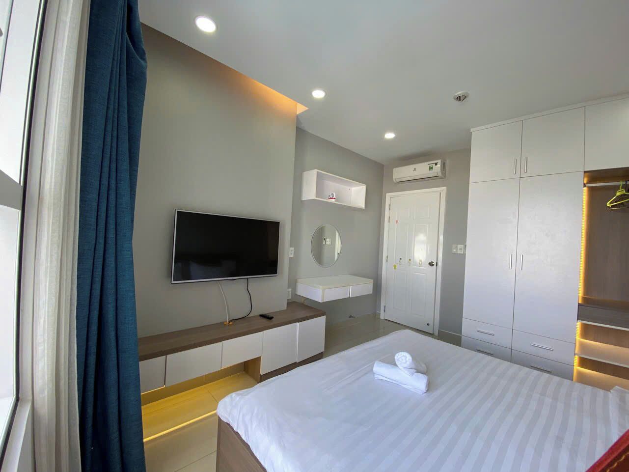 Habitación de hotel con cama, televisor, mesita de noche, espejo, armario y ventana con cortinas.