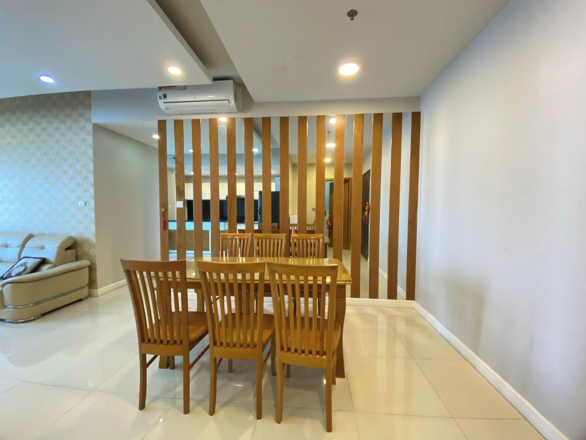 A modern dining area with a wooden table and chairs, a sofa, and a decorative wooden partition.