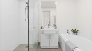 A modern bathroom with a glass-enclosed shower, a white sink with a mirror above, and a bathtub with a towel. - Walk to Beach and shops, Spacious, Ocean Views (Ocean Grove)