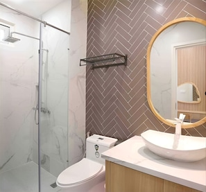 Un baño moderno con cabina de ducha de vidrio, inodoro blanco, tocador de mármol con lavamanos y salpicadero con motivo de espiga.