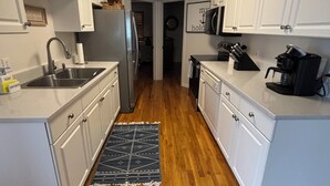 A narrow kitchen with white cabinets, a stainless steel sink, and a coffee maker.