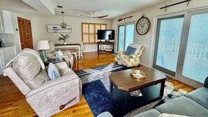 A spacious living room with a ceiling fan, a television, and a dining area with a table and chairs.