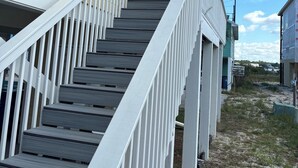 A wooden staircase leading to a house with a beige exterior and white railings.