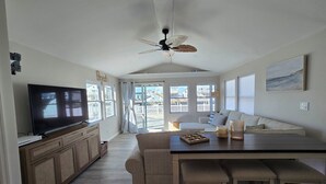 A spacious living area with a large flat-screen TV, a ceiling fan, and a view of the beach through the sliding glass doors. - Beautifully updated waterfront home great for families & friends +beach badges. (Little Egg Harbor Township)