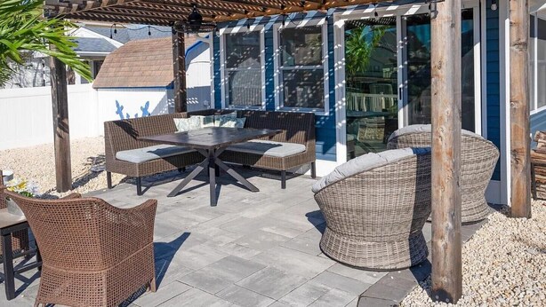 An outdoor patio with wicker furniture, a pergola, and a glass enclosure. - Beautifully updated waterfront home great for families & friends +beach badges. (Little Egg Harbor Township)