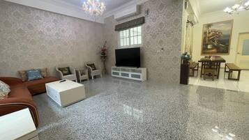 A spacious living room with a large TV, a sofa, a coffee table, and a dining area with a table and benches.