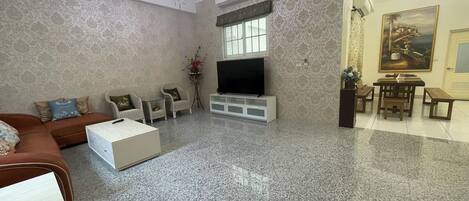 Un salon spacieux avec une grande télévision, un canapé, une table basse et un coin repas comprenant une table et des bancs.