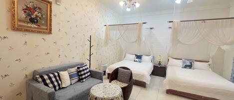 A room with a sofa, two beds, a small table, and a decorative painting.