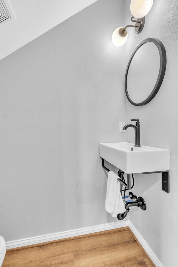 Un baño con un lavamanos blanco, un espejo redondo y un perchero para toallas.