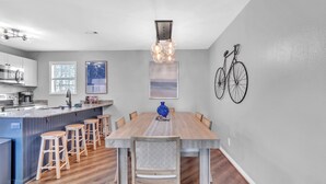 Una cocina moderna con una isla grande, taburetes de madera y una mesa de comedor con un centro de mesa en una jarra.