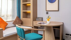 Une pièce moderne avec un fauteuil de couleur turquoise, une table en bois, une bibliothèque et une œuvre d’art encadrée accrochée au mur.