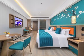 Una habitación de hotel moderna con una cama grande, un escritorio, una silla, un televisor montado en la pared y un mural decorativo.