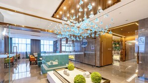 Un hall d’hôtel moderne avec une cloison en verre, un espace salon et des luminaires décoratifs suspendus.
