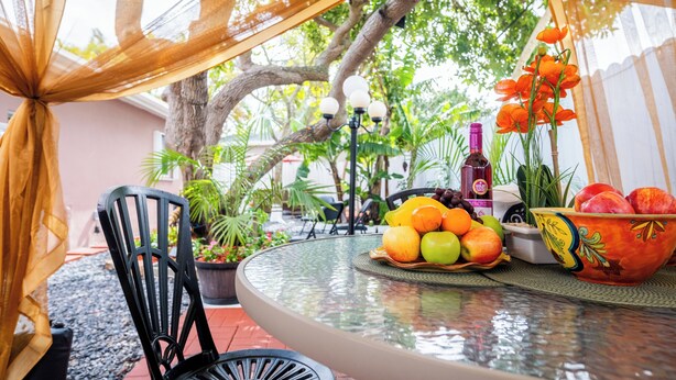 A round glass table with a fruit bowl, a bottle, and a potted plant.