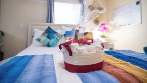 A bed with a striped blanket, a basket of toiletries, and a welcome sign on the wall.