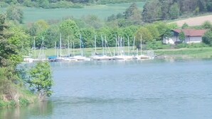 Um lago com barcos à vela atracados, rodeado por vegetação e um pequeno edifício.
