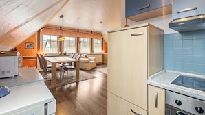 Cozinha com fogão, forno e geladeira, área de jantar com mesa e cadeiras, e janela com cortinas.